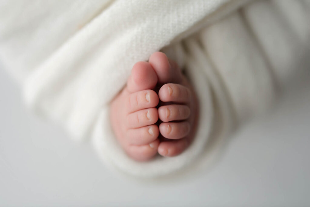 Close-up of a newborn baby’s feet wrapped snugly in a soft, white blanket, showing tiny toes and smooth skin in gentle light—captured by a skilled phoenix maternity photographer.