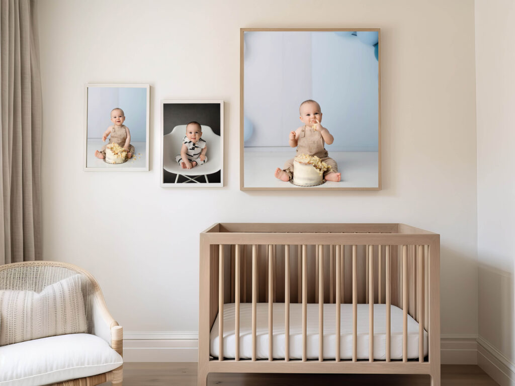 Wooden crib in a nursery with three framed baby photos above it, captured by a Phoenix maternity photographer; in two, the baby enjoys cake in a diaper, and in the third, sits on a chair. Another chair is placed to the side.