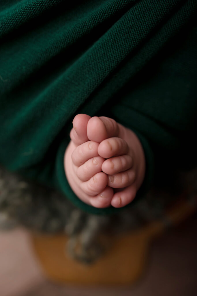 Close-up of a newborn baby's tiny feet, nestled together and partially wrapped in a dark green blanket. Captured by a skilled Phoenix newborn photographer, the baby's soft, delicate skin is beautifully highlighted.