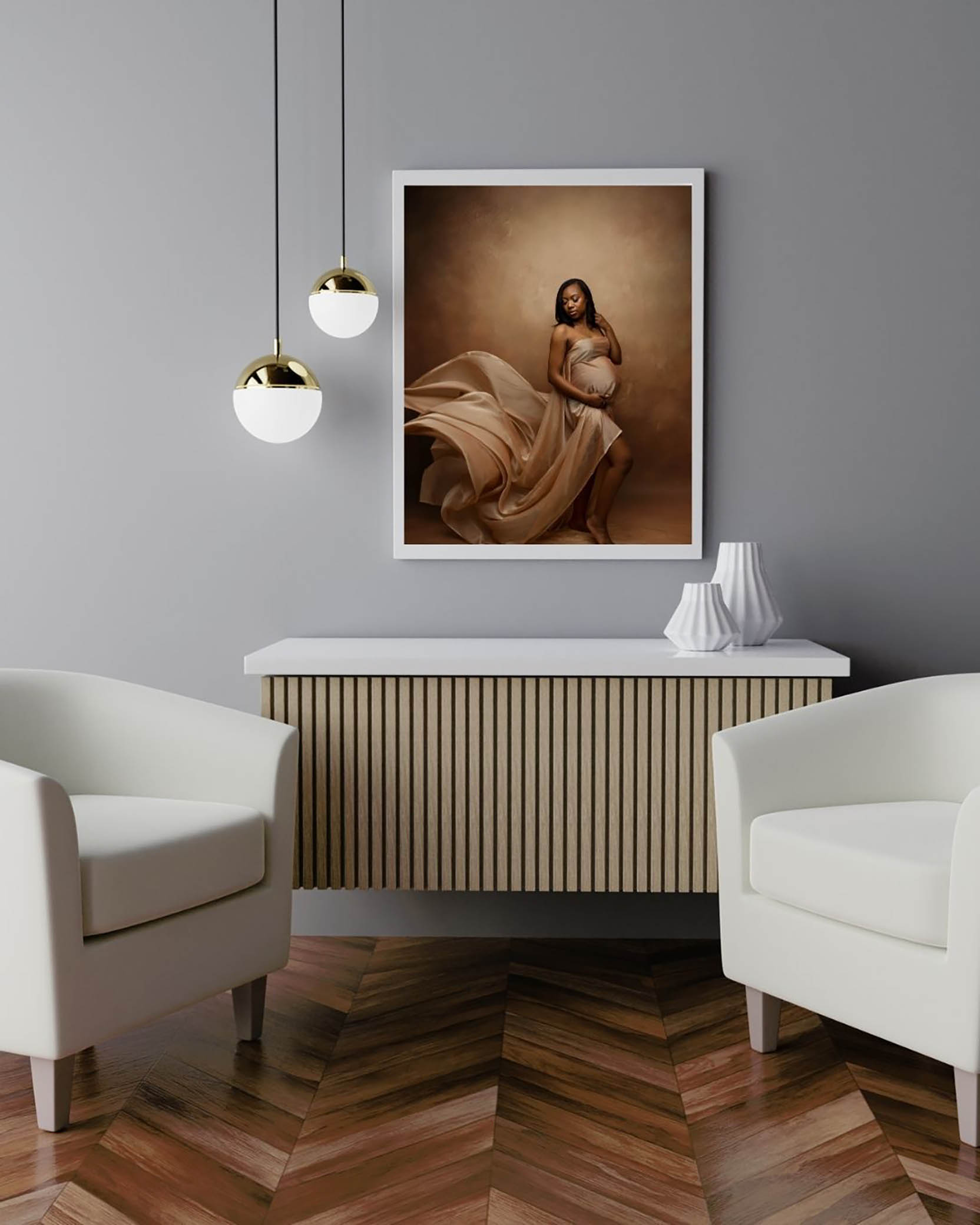 A modern room with two white armchairs, a light wood sideboard, and pendant lights. A framed photo by a Phoenix maternity photographer of a woman in a flowing dress hangs on the gray wall above the sideboard.